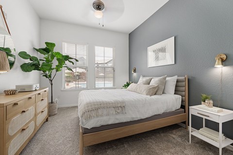 A bedroom with a bed, nightstand, and a plant.