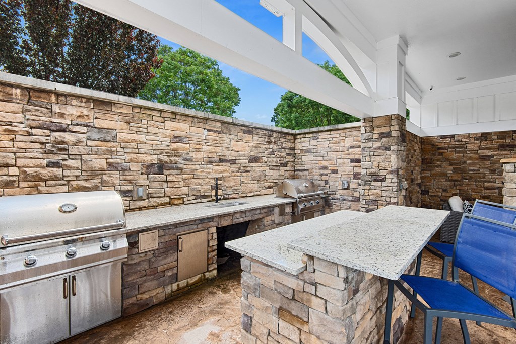 an outdoor kitchen with a grill and a bar with blue chairs