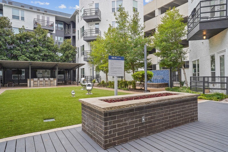 a grassy courtyard with a brick wall in front of an apartment building