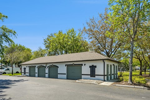 A white building with a brown roof and green trim is surrounded by trees and a parking lot.