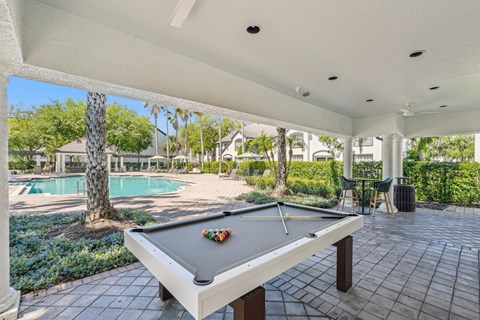 A pool table is in the middle of a patio with a pool table cloth and balls on it.