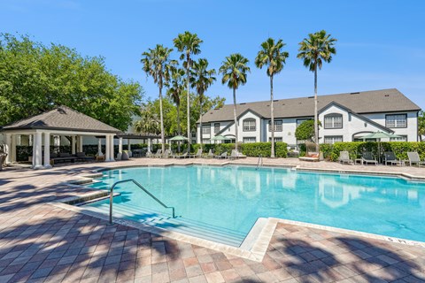 A pool surrounded by palm trees and a building.
