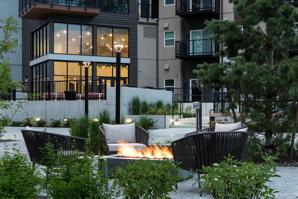 a patio with a fire pit and chairs in front of a building