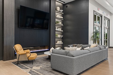 A modern living room with a grey sofa, a yellow chair, and a black television mounted on the wall.