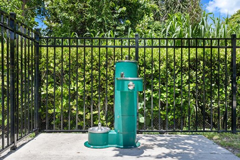 A green water pump is on a concrete slab in front of a black fence.