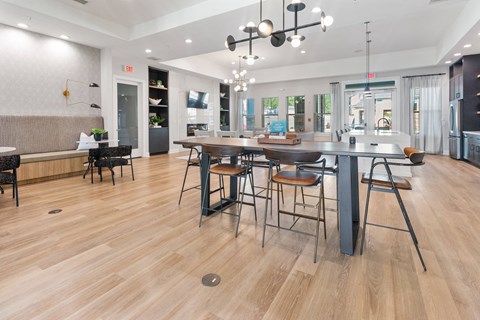 a resident clubhouse with a large table with stools and a kitchen area in the background