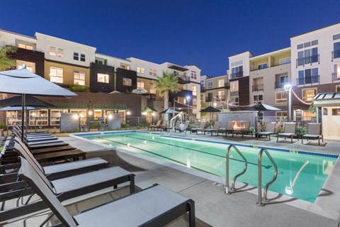 a swimming pool at night with an apartment building in the background