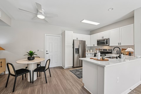 A kitchen with a table and chairs in the foreground and a refrigerator, microwave, and oven in the background.