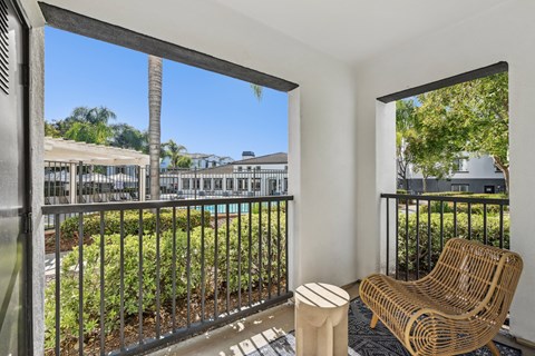 A balcony with a chair and table overlooking a pool and buildings.