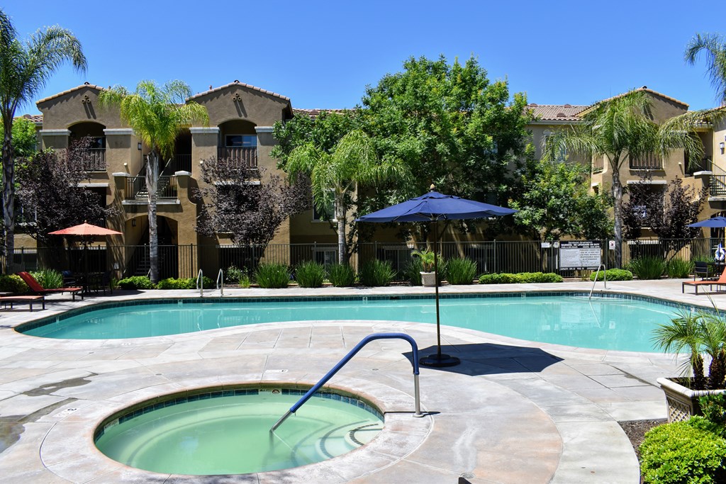 a swimming pool with an umbrella in front of an apartment building