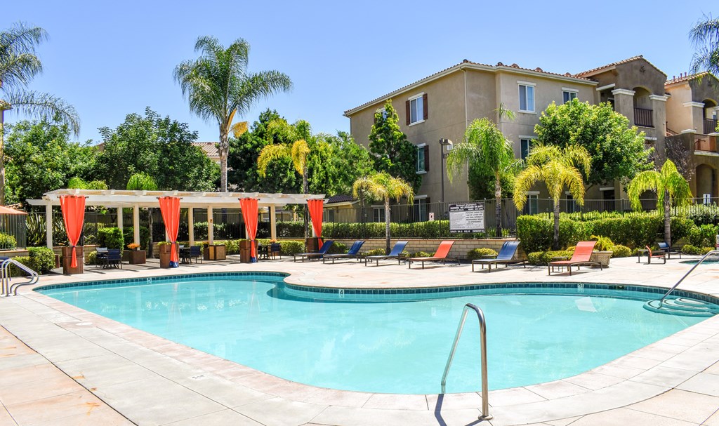 A swimming pool surrounded by a red canopy and chairs.