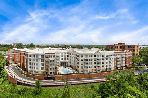 A large multi-story building with a pool in the middle of a green landscape.