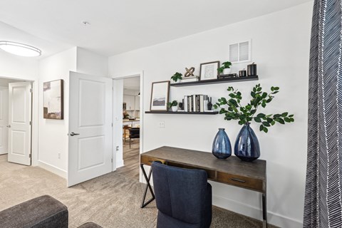 a living room with a desk and chairs and a hallway with a door and a