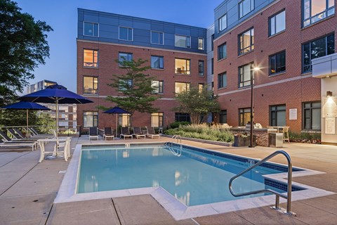 A swimming pool surrounded by lounge chairs and umbrellas in front of a brick building.