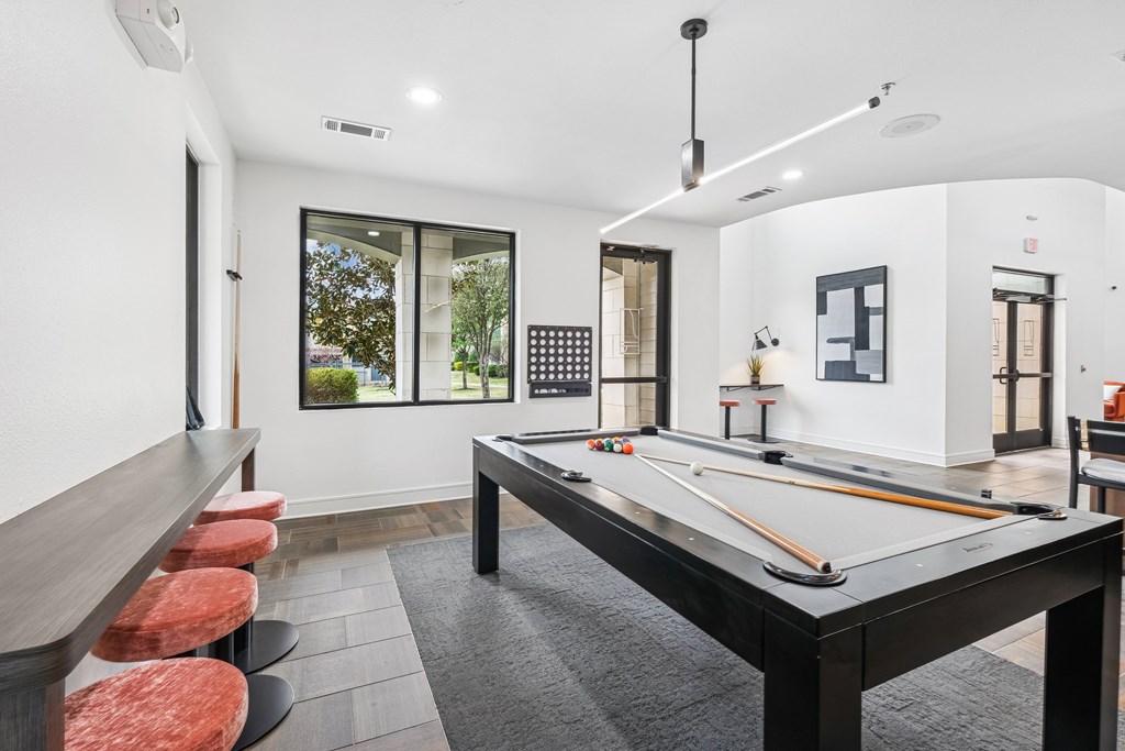 A pool table is in the middle of a room with a white ceiling and a window.
