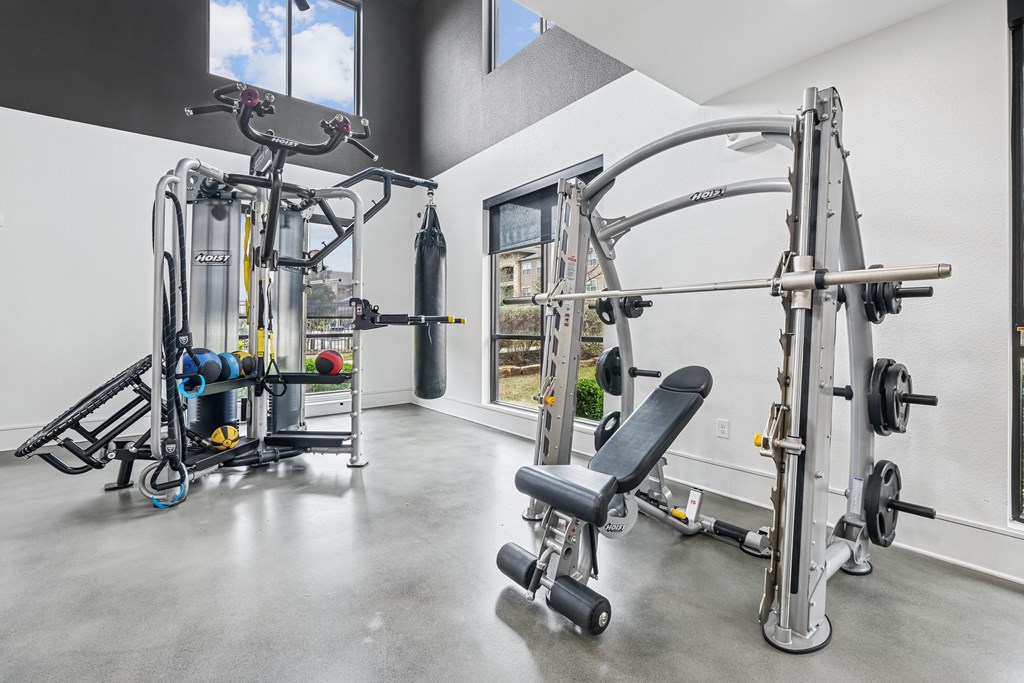 A gym with a variety of equipment including a leg press machine, a seated calf raise machine, a chest press machine, a squat rack, a bench, and a barbell.