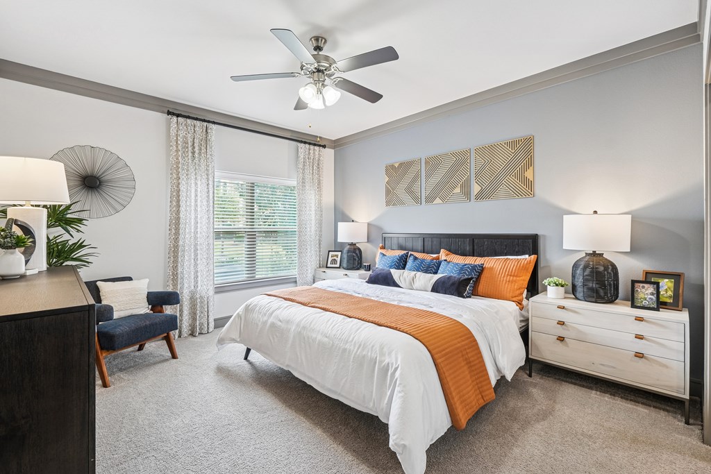 A bedroom with a large bed, a ceiling fan, and a nightstand with a lamp.