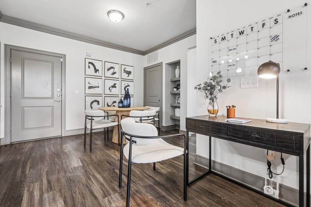 A white wall with a calendar and a desk with a chair.