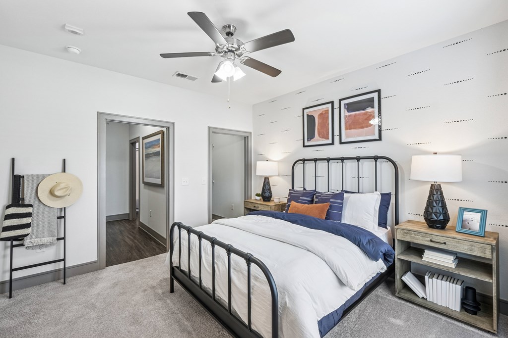 A bedroom with a large bed, a ceiling fan, and a nightstand with a lamp.
