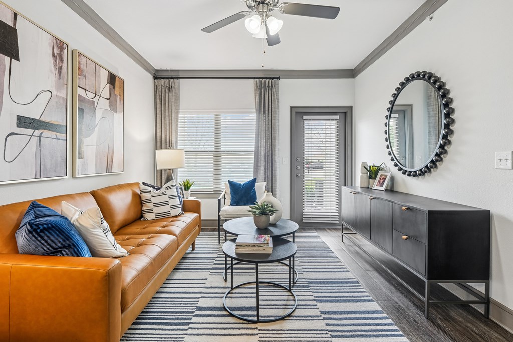A living room with a brown leather couch, a round table, and a ceiling fan.