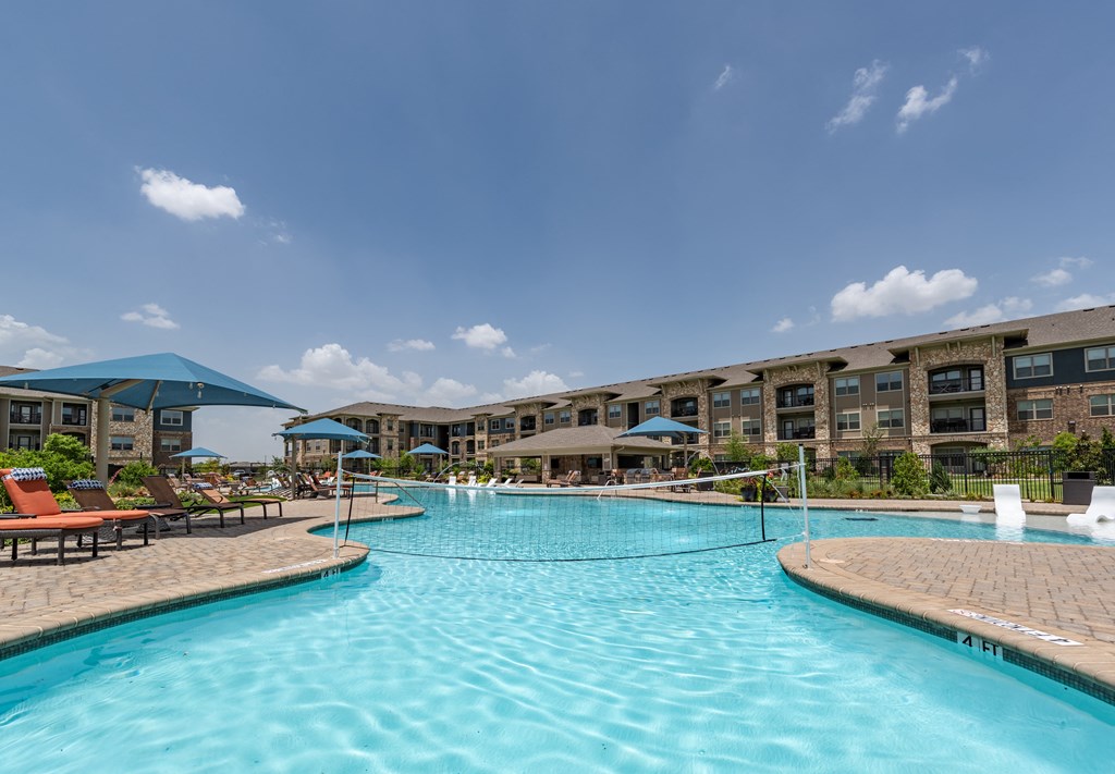 a large pool with lounge chairs and umbrellas in front of a building
