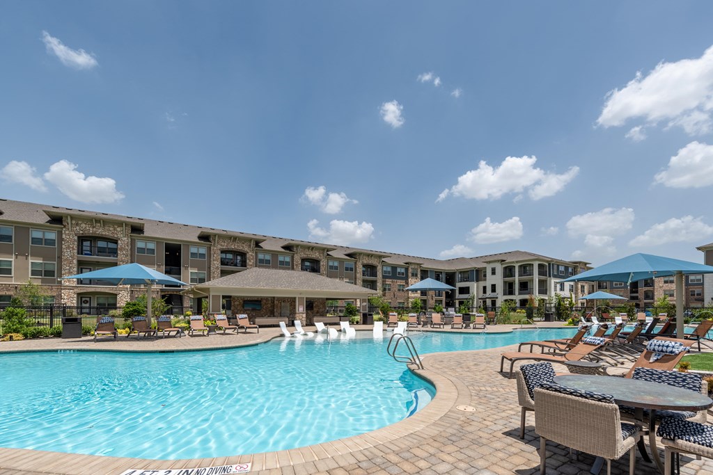 a swimming pool with lounge chairs and umbrellas in front of a building