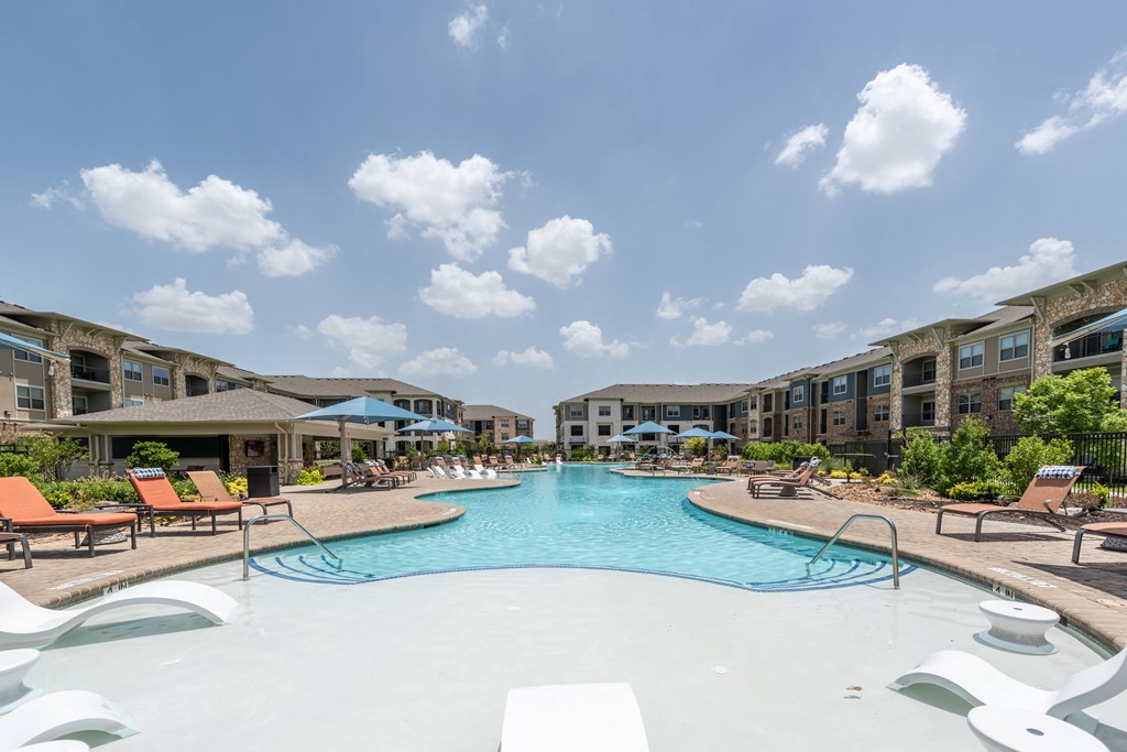 a swimming pool with lounge chairs and umbrellas in front of an apartment building