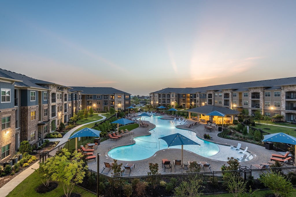 an aerial view of the resort style pool with lounge chairs and umbrellas at dusk
