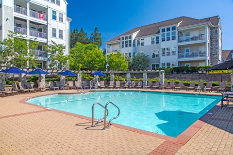 A swimming pool surrounded by a brick patio and lounge chairs.