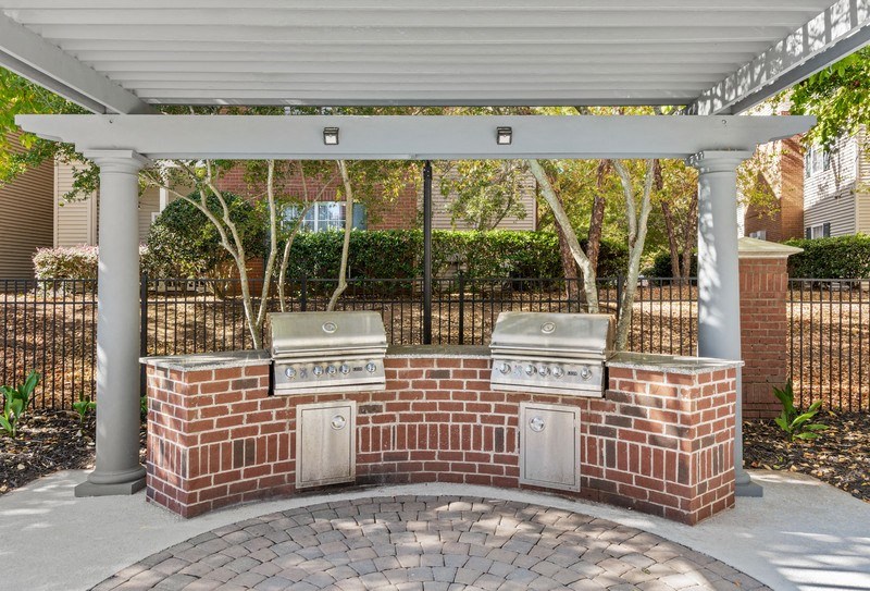a brick barbecue area with two bbq grills under a white awning