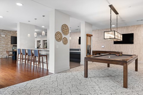 A pool table is in the middle of a room with a bar and a TV.