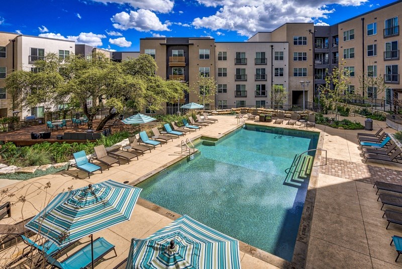 a pool with lounge chairs and umbrellas in front of an apartment building