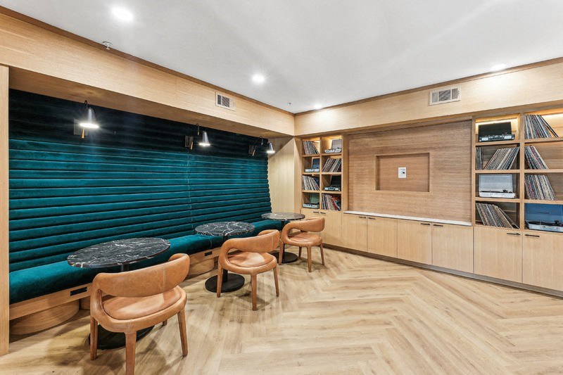 a library with wooden floors and a turquoise bench and tables