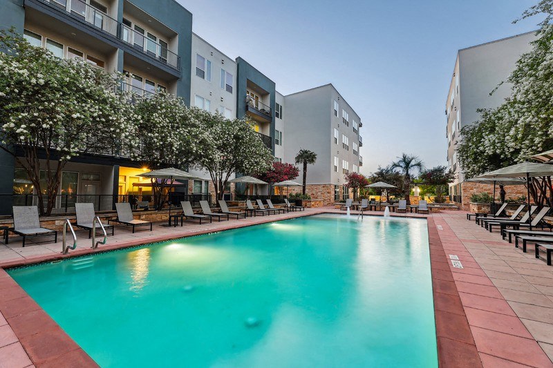 a swimming pool with chairs and buildings in the background