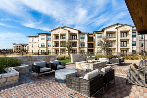 an outdoor patio with chairs and a fire pit in front of an apartment building