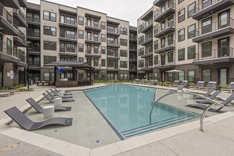 A swimming pool surrounded by lounge chairs in front of apartment buildings.