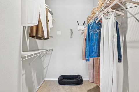 a walk in closet with clothes hanging in it and a white closet door