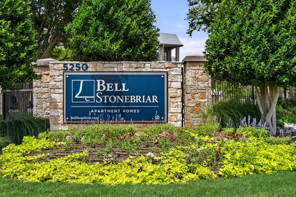 a sign for bell stonerbar apartments in front of a stone wall with flowers