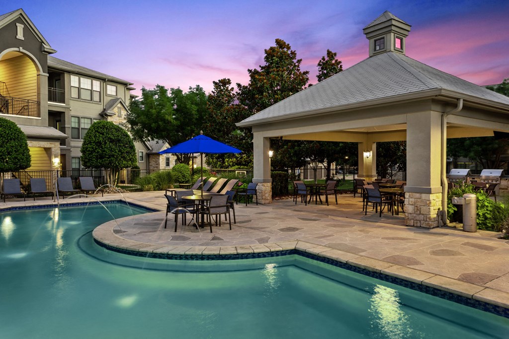 a swimming pool with a pavilion and patio with tables and chairs