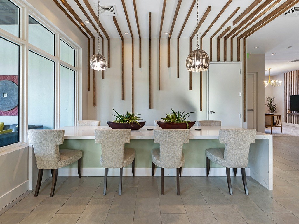 a dining area with a long table with chairs and pendant lights hanging from the ceiling