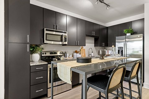 A kitchen with black cabinets and a stainless steel refrigerator.