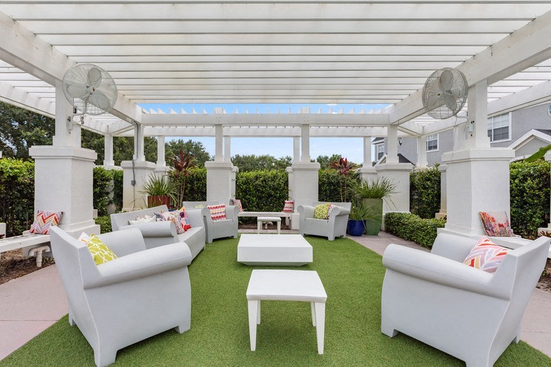 a pergola with white furniture and a green lawn