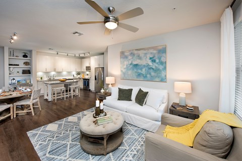 A living room with a white couch, a round ottoman, and a painting on the wall.