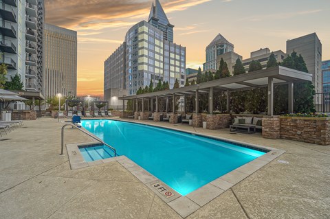 A swimming pool with seating around it and tall buildings in the background.