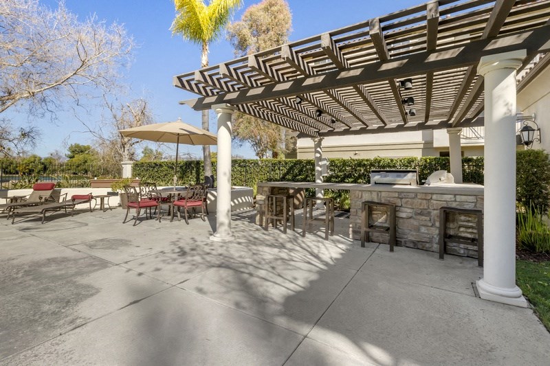 a patio with a grill and tables and a pergola