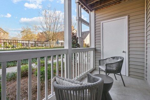 A patio with a white chair and a wicker chair with a table in between.