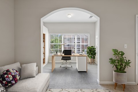 A room with a white couch, a desk with a computer, and a potted plant.