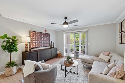 A living room with a grey couch, a grey armchair, a wooden coffee table, a potted plant, and a fan.