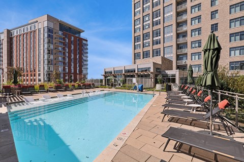 A large swimming pool with lounge chairs and umbrellas in front of apartment buildings.
