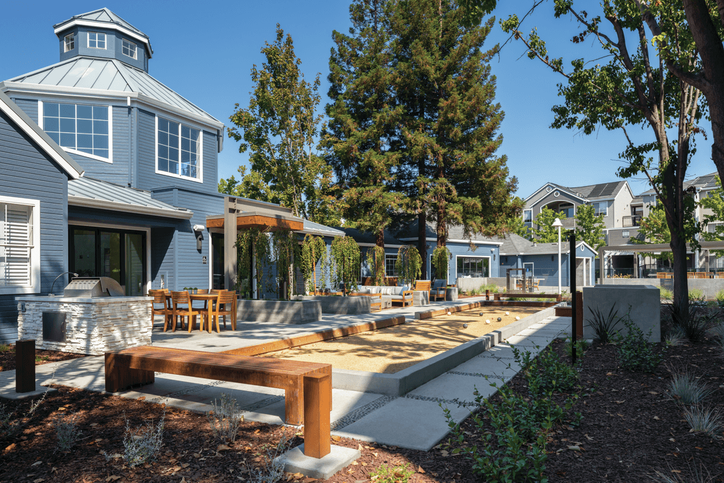 A modern house with a blue roof and a white exterior is surrounded by trees and has a wooden deck.